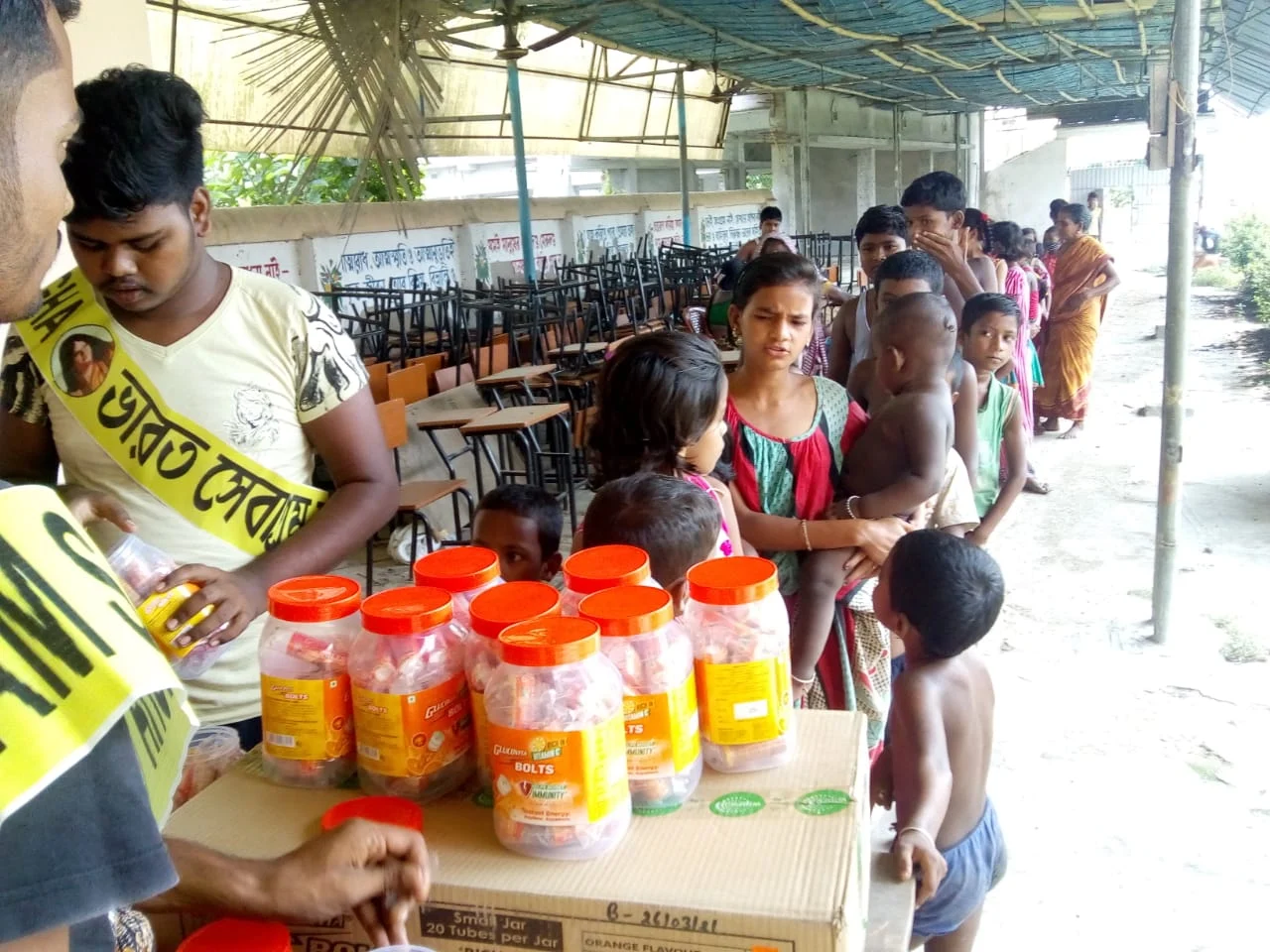 Relief Work: A Bharat Sevashram Sangha volunteer handing out relief supplies to children queuing at a distribution point