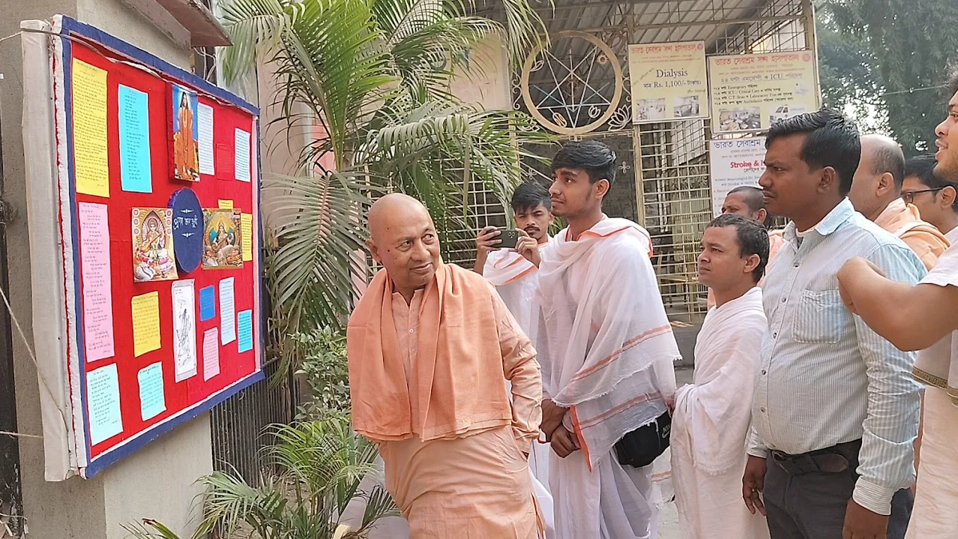 Community: A monk speaking with visitors beside a display board of photographs and charts