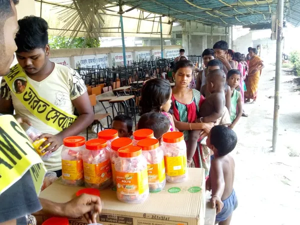 Relief Work: A Bharat Sevashram Sangha volunteer handing out relief supplies to children queuing at a distribution point