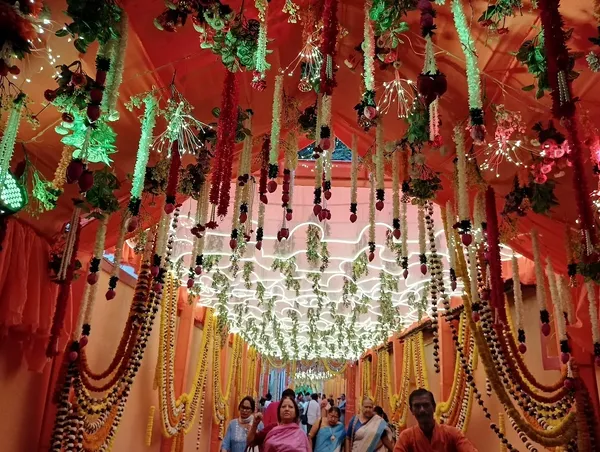Festivals & Observances: A festival corridor hung with marigold garlands and lights, with devotees walking through