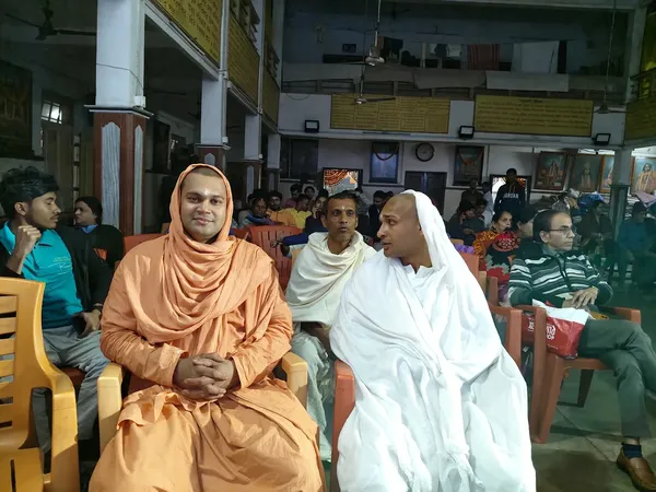 Community: A monk and a nun seated together at a gathering, with devotees behind them