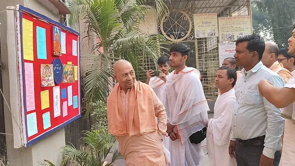 Community: A monk speaking with visitors beside a display board of photographs and charts
