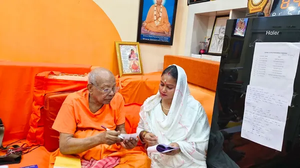 Community: A senior monk seated in conversation with a devotee, framed portraits on the wall behind