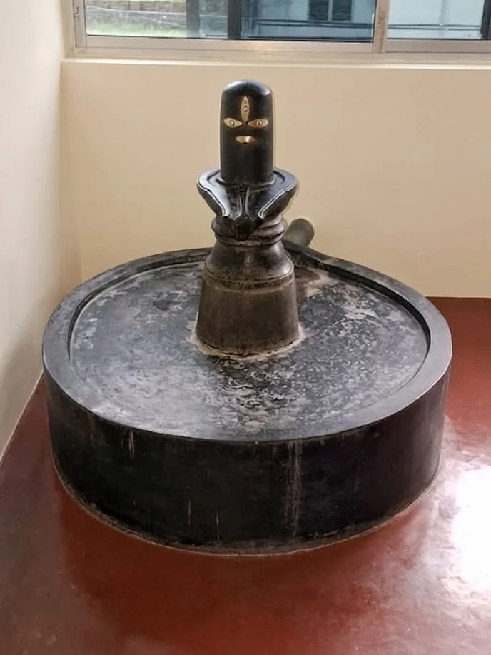 A black stone Shiva lingam on its circular base in the ashram shrine, lit by a window